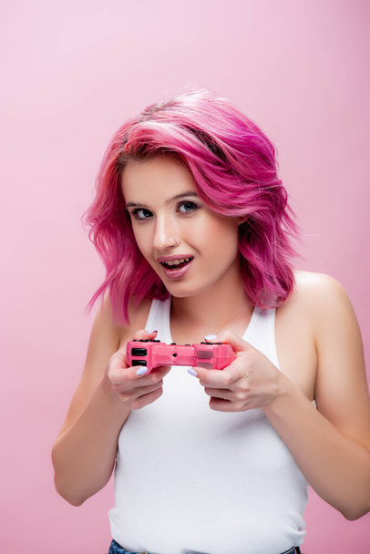 KYIV, UKRAINE - JULY 29, 2020: young woman with colorful hair holding joystick isolated on pink - Foto, Imagem