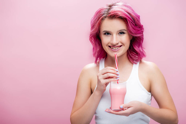 mujer joven con pelo colorido sosteniendo batido de fresa con paja aislada en rosa - Foto, Imagen
