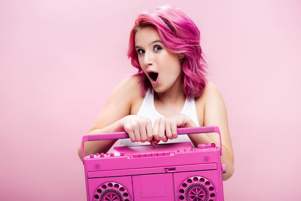choqué jeune femme avec des cheveux colorés tenant magnétophone peint isolé sur rose - Photo, image