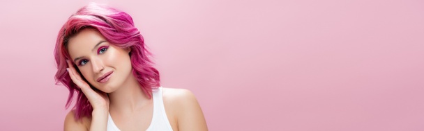 mladá žena s barevnými vlasy a make-up dotek tvář izolované na růžové, panoramatický záběr - Fotografie, Obrázek