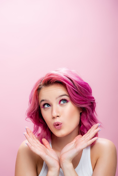 zaskoczona młoda kobieta z kolorowymi włosami i makijaż pozowanie z rąk blisko twarzy odizolowane na różowy - Zdjęcie, obraz