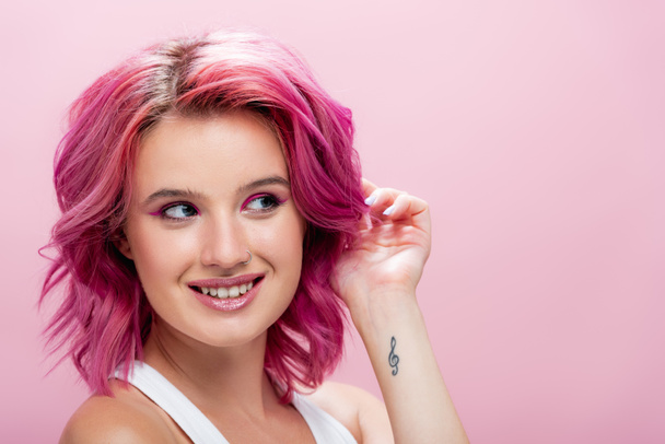 jovem com cabelo colorido e maquiagem posando com a mão perto do rosto isolado em rosa - Foto, Imagem