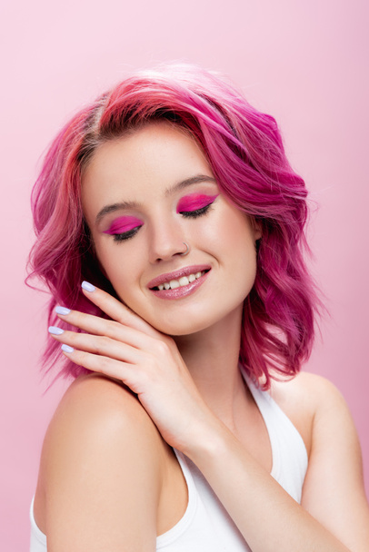 молода жінка з барвистим волоссям і макіяжем позує рукою біля обличчя ізольовано на рожевому
 - Фото, зображення