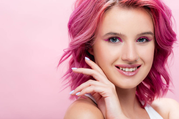 junge Frau mit buntem Haar und Make-up posiert mit händennahem Gesicht isoliert auf rosa - Foto, Bild