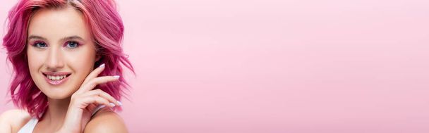 young woman with colorful hair and makeup posing with hand near face isolated on pink, panoramic shot - Photo, Image