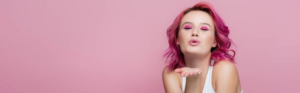 mladá žena s barevnými vlasy foukání polibek izolované na růžové, panoramatický výstřel - Fotografie, Obrázek