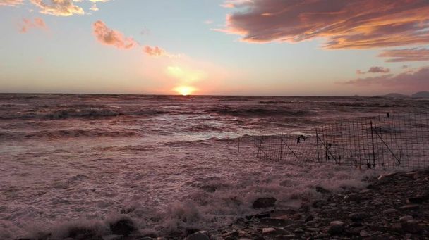 μια ματιά στην παραλία το ηλιοβασίλεμα, μια μαγική στιγμή στην οποία όλα χρωματίζονται με φωτεινά χρώματα. τα σύννεφα πλαισιώνουν το θαλάσσιο τοπίο και ο ήλιος σιγά σιγά εξαφανίζεται στον ορίζοντα - Φωτογραφία, εικόνα