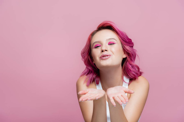 mujer joven con pelo colorido soplado beso aislado en rosa - Foto, Imagen