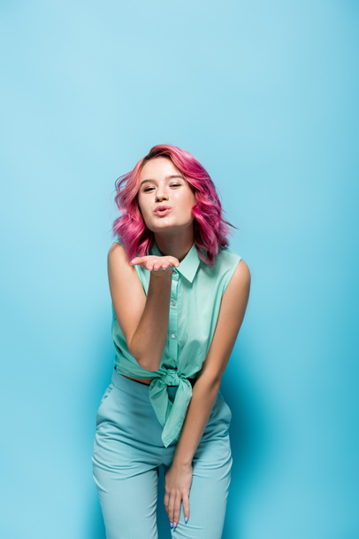 mladá žena s růžovými vlasy foukání polibek na modrém pozadí - Fotografie, Obrázek