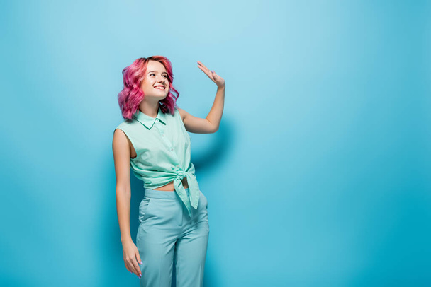 young woman with pink hair waving hand on blue background - Photo, Image