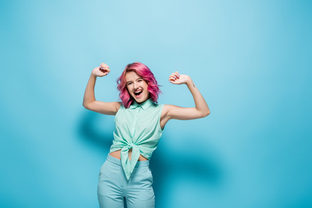 excited young woman with pink hair gesturing on blue background - Foto, immagini
