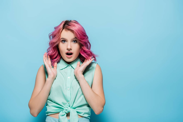 mujer joven sorprendida con el pelo rosa y la boca abierta sobre fondo azul - Foto, imagen