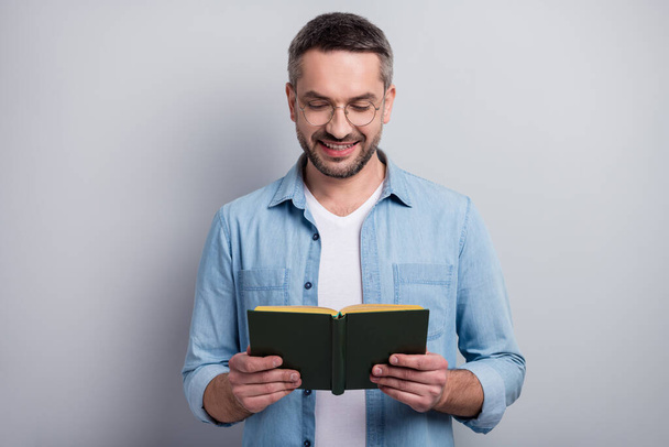 Close-up portrait of his he nice attractive cheerful cheery focused gray-haired guy reading interesting paper book isolated over gray light pastel color background - Fotoğraf, Görsel