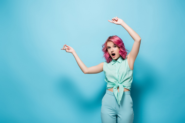 shocked young woman with pink hair pointing aside on blue background - Foto, Imagem