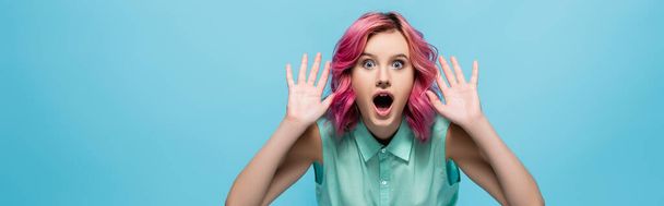 schockierte junge Frau mit rosafarbenen Haaren, die Hände isoliert auf blauem, panoramischem Foto zeigt - Foto, Bild