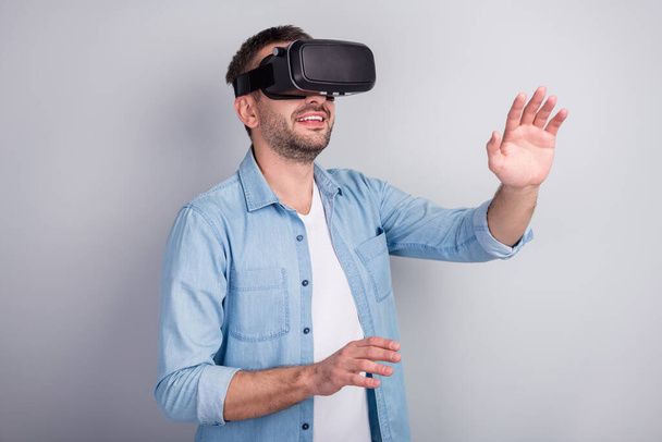 Close-up portrait of his he nice attractive cheerful dreamy guy wearing VR helmet headset playing game dream walking going touching space isolated over gray light pastel color background - Foto, imagen