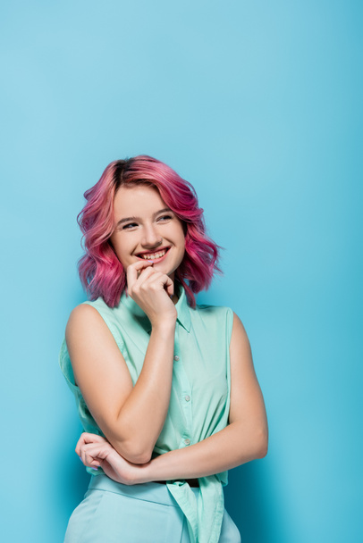 νεαρή γυναίκα με ροζ μαλλιά χαμογελώντας και φλερτάροντας σε μπλε φόντο - Φωτογραφία, εικόνα