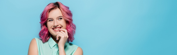 young woman with pink hair smiling and flirting isolated on blue, panoramic shot - Foto, afbeelding