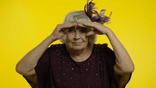 Oudere oude vrouw kijkt ver weg met hand over ogen, zoekt op afstand, drukt verbazing uit - Foto, afbeelding