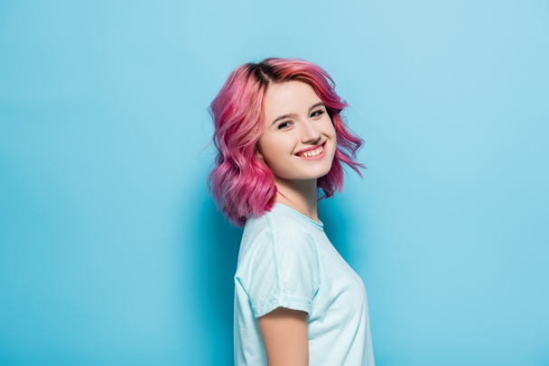 oldalnézetben fiatal nő rózsaszín haj mosolygós kék háttér - Fotó, kép