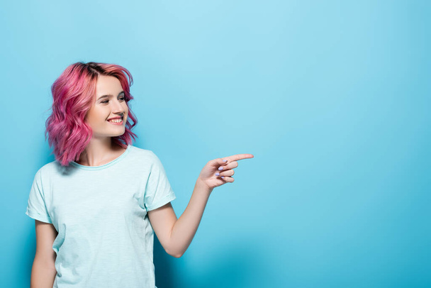 young woman with pink hair pointing aside on blue background - Photo, image