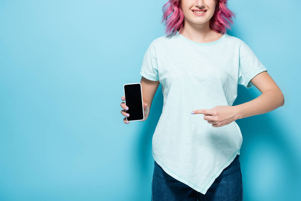 cropped view of young woman with pink hair pointing at smartphone with blank screen on blue background, panoramic shot - Photo, image