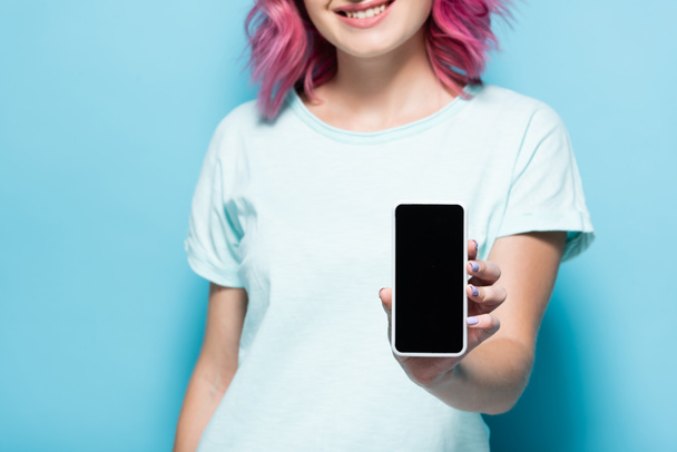 przycięty widok młodej kobiety z różowymi włosami gospodarstwa smartfon z czystym ekranem na niebieskim tle - Zdjęcie, obraz