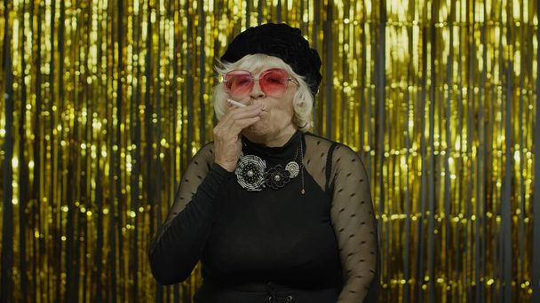 Ouderen stijl volwassen oma in de mode zwarte kleren in zonnebril poseren, rook sigaret - Foto, afbeelding