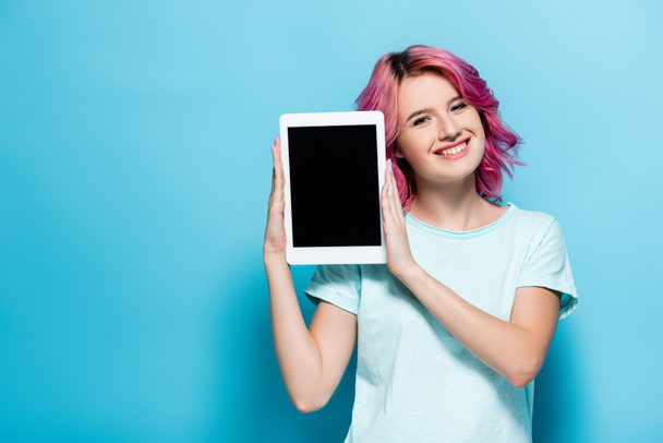 young woman with pink hair presenting digital tablet with blank screen on blue background - Foto, Bild