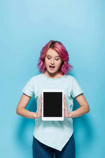 excited young woman with pink hair presenting digital tablet with blank screen on blue background - Fotoğraf, Görsel