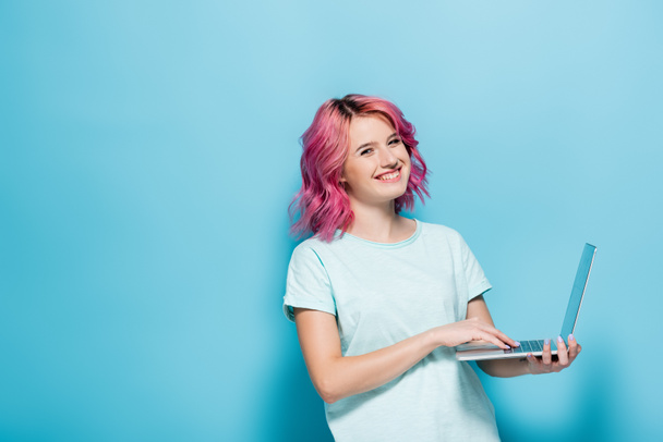 Nuori nainen vaaleanpunaiset hiukset kannettavan tietokoneen avulla sinisellä taustalla - Valokuva, kuva