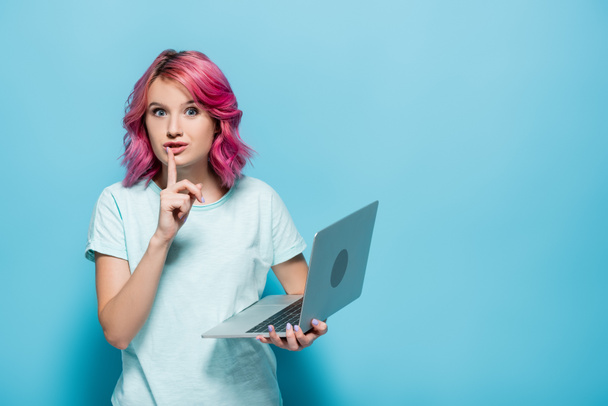 young woman with pink hair holding laptop and showing shh gesture on blue background - Photo, Image