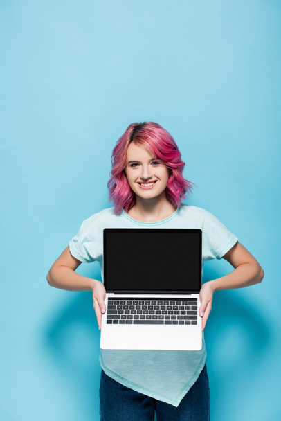 jeune femme avec les cheveux roses montrant ordinateur portable avec écran blanc sur fond bleu - Photo, image