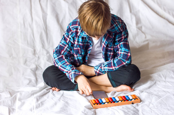 Un garçon un écolier fait des tâches sur l'arithmétique mentale sur un abaque à la maison, l'apprentissage en ligne à distance pendant la quarantaine du coronavirus, développement mental supplémentaire - Photo, image