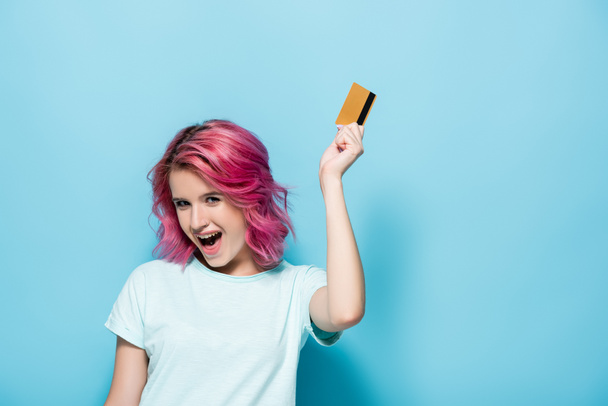 excité jeune femme avec les cheveux roses tenant carte de crédit sur fond bleu - Photo, image
