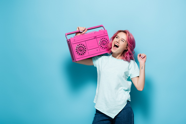 young woman with pink hair holding vintage tape recorder on blue background - Foto, Bild