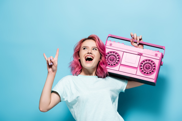 izgatott fiatal nő rózsaszín haj gazdaság vintage magnó és bemutató rock jel kék háttér - Fotó, kép