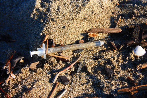 επικίνδυνες χρησιμοποιημένες σύριγγες εγκαταλελειμμένες στην παραλία στη μέση άλλων ακαθαρσιών και σκουπιδιών - Φωτογραφία, εικόνα