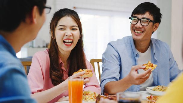 Χαρούμενοι νεαροί φίλοι τρώνε στο σπίτι. Ασιατικό οικογενειακό πάρτι τρώγοντας πίτσα και γελώντας απολαμβάνοντας το γεύμα, ενώ κάθονται στο τραπέζι μαζί στο σπίτι. Εορτασμός διακοπών και ομαδικότητας. - Φωτογραφία, εικόνα