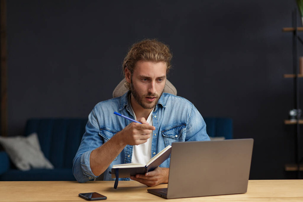 Studying online,online courses.Business concept.Young handsome curly smiling man with long hair studying in home with laptop.Business portrait of handsome manager sitting at workplace - Fotografie, Obrázek