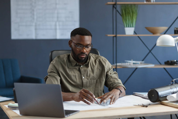 Afro-American architect working in office with blueprints.Engineer inspect architectural plan, sketching a construction project. Portrait of black handsome man sitting at workplace. Business concept - Φωτογραφία, εικόνα