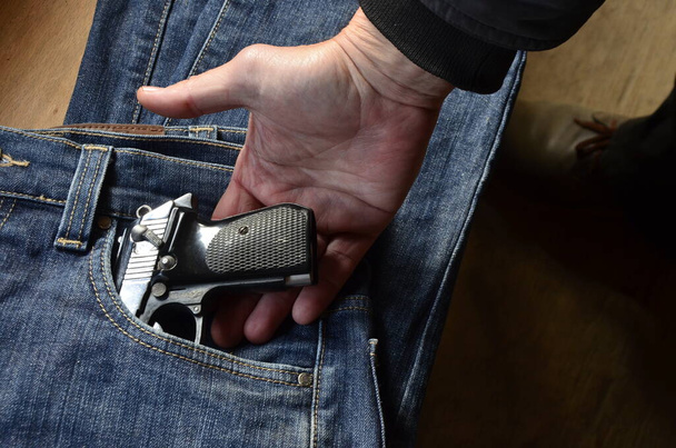 Gun in a pocket of jeans trousers fighting loaded.Pistol in the pocket of jeans. - Photo, Image
