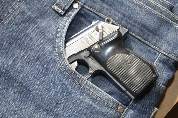 Gun in a pocket of jeans trousers fighting loaded.Pistol in the pocket of jeans. - Photo, Image