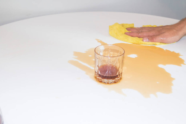 A fickó letörli a fehér asztalt egy sárga ronggyal a kiömlött teából. - Fotó, kép