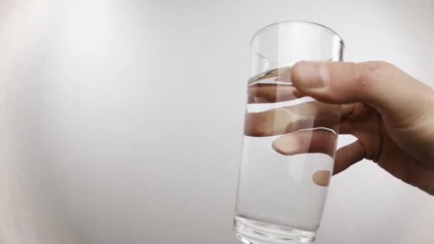 L'uomo tiene in mano il vetro trasparente e beve acqua nello studio - Filmati, video