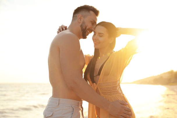 Happy young couple on beach at sunset - Foto, afbeelding