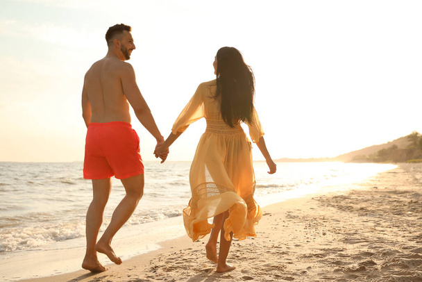 Happy couple walking together on beach at sunset, back view - Φωτογραφία, εικόνα