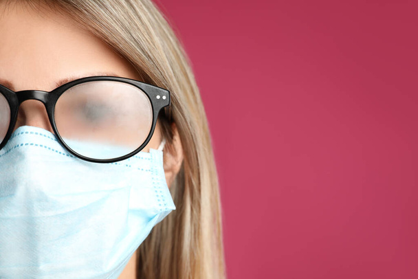 Woman with foggy glasses caused by wearing disposable mask on pink background, space for text. Protective measure during coronavirus pandemic - Photo, Image