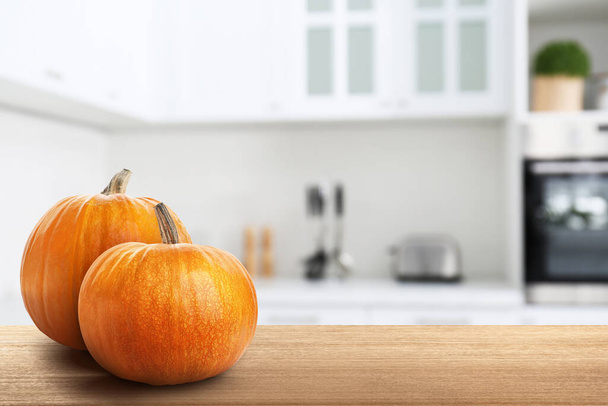 Fresh pumpkins on wooden table in kitchen. Space for text - Фото, изображение