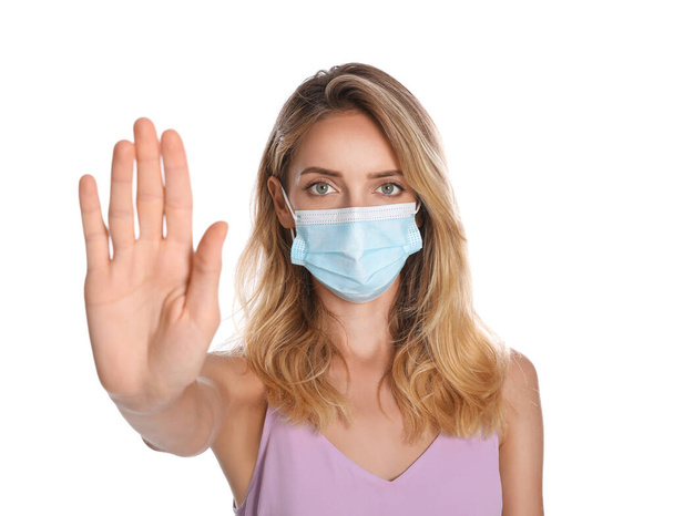 Woman in protective face mask showing stop gesture on white background. Prevent spreading of coronavirus - Fotografie, Obrázek